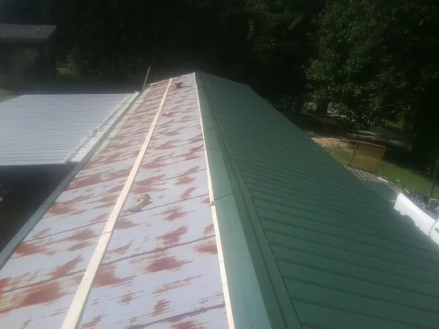 Old rusted panels beside newly installed green metal roofing — Wind Damage Roof Repair by Roofing Brothers in Worton