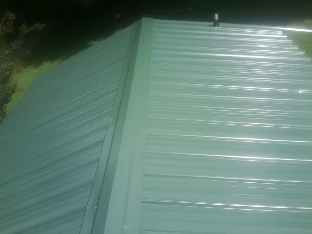 New green metal panels meeting at the ridge of a roof — Flat Roof Repair work by our crew in Worton