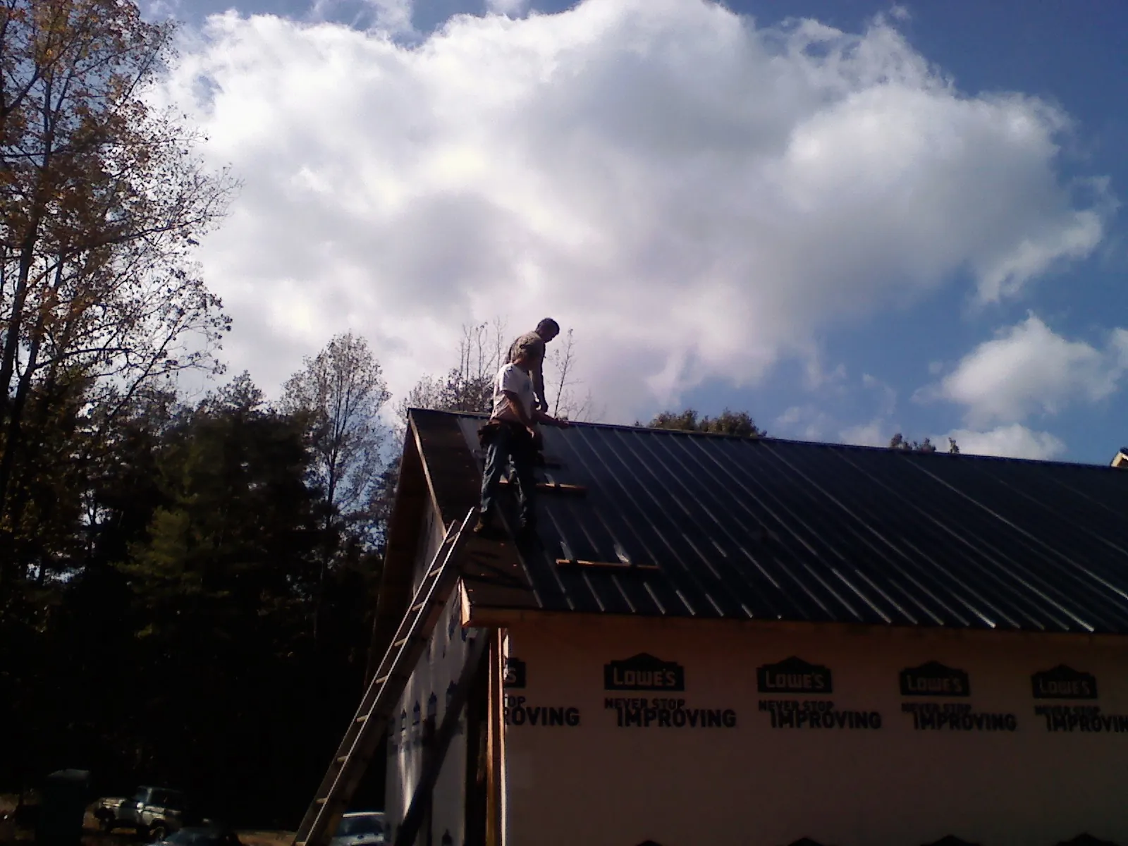 Roofer fastening dark metal panels high against a cloudy sky, from a Roof Inspection job in Worton